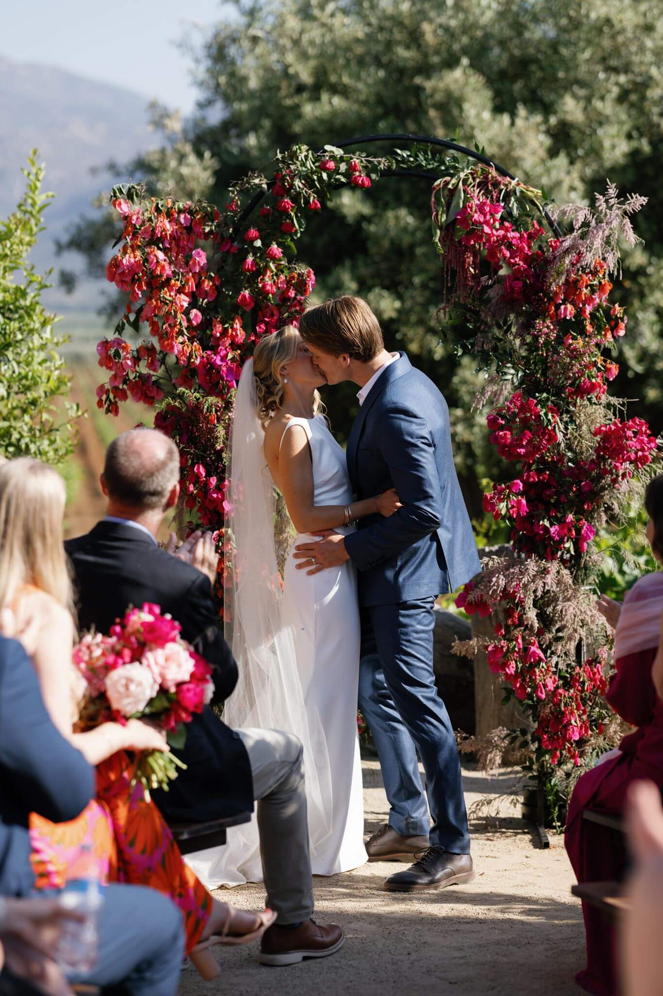 Bride and groom sharing their first kiss beneath the floral ceremony arch.