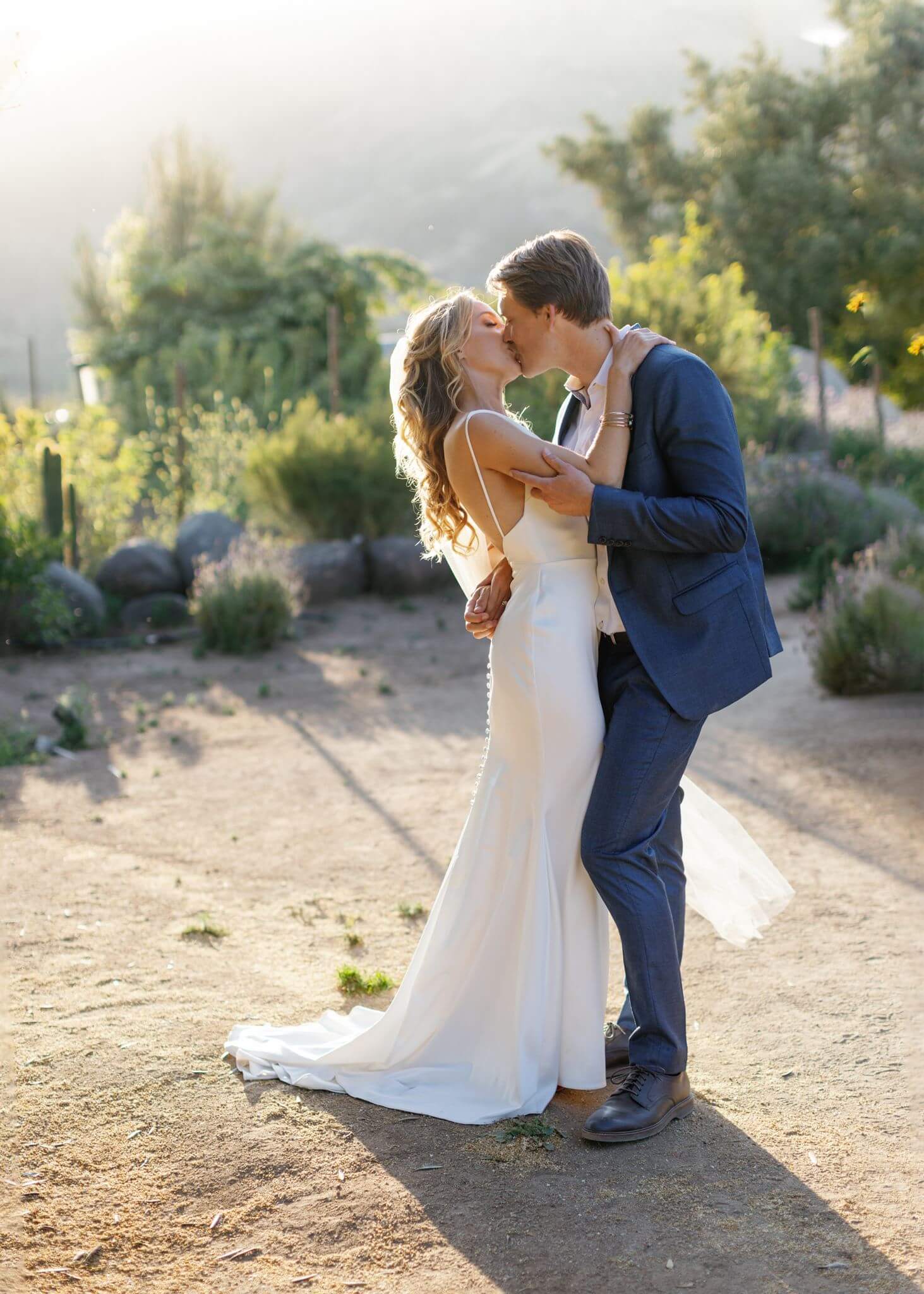Bride and groom kissing on a garden path during golden-hour wedding portraits.