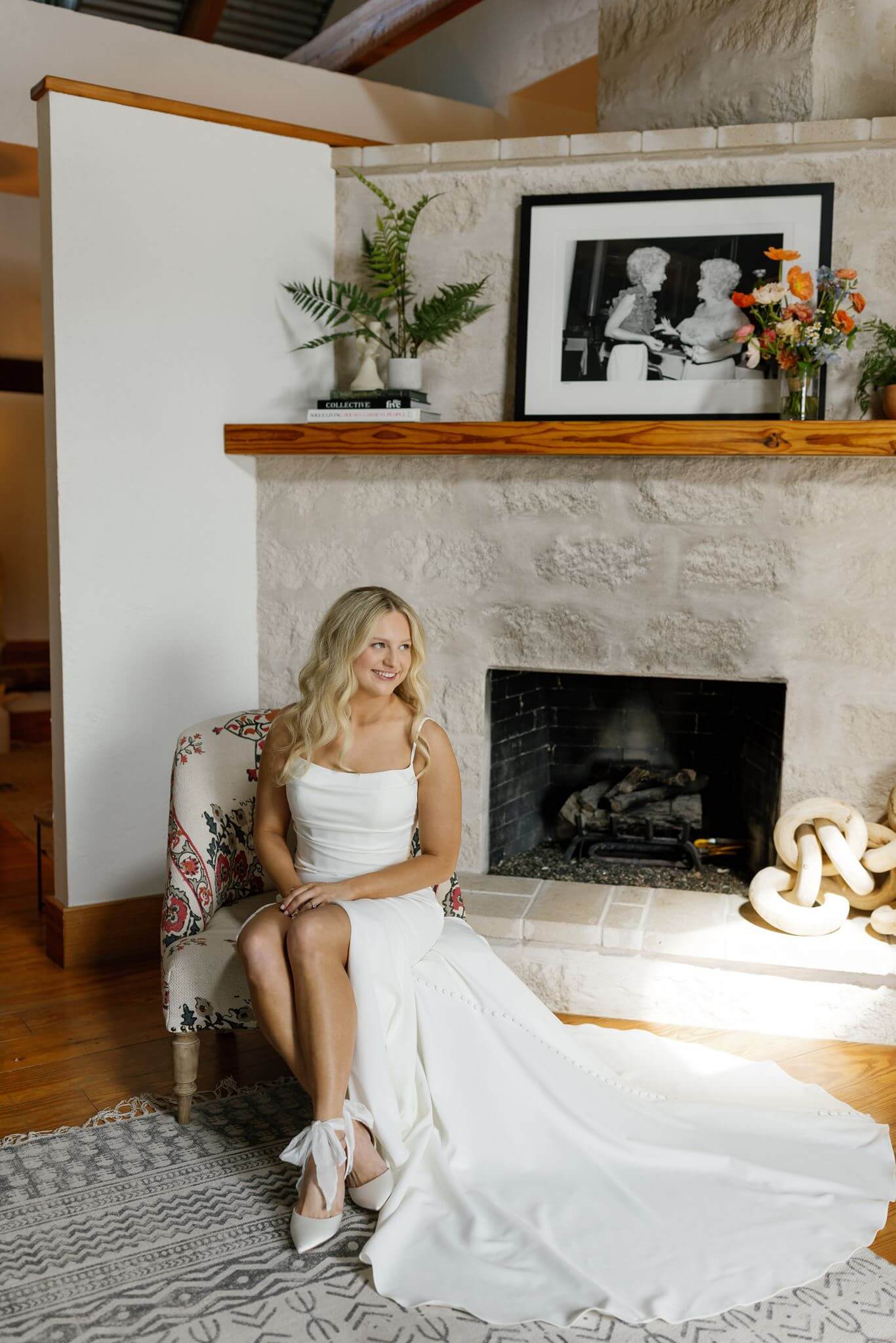 Bride sitting by a stone fireplace in her wedding gown, smiling softly