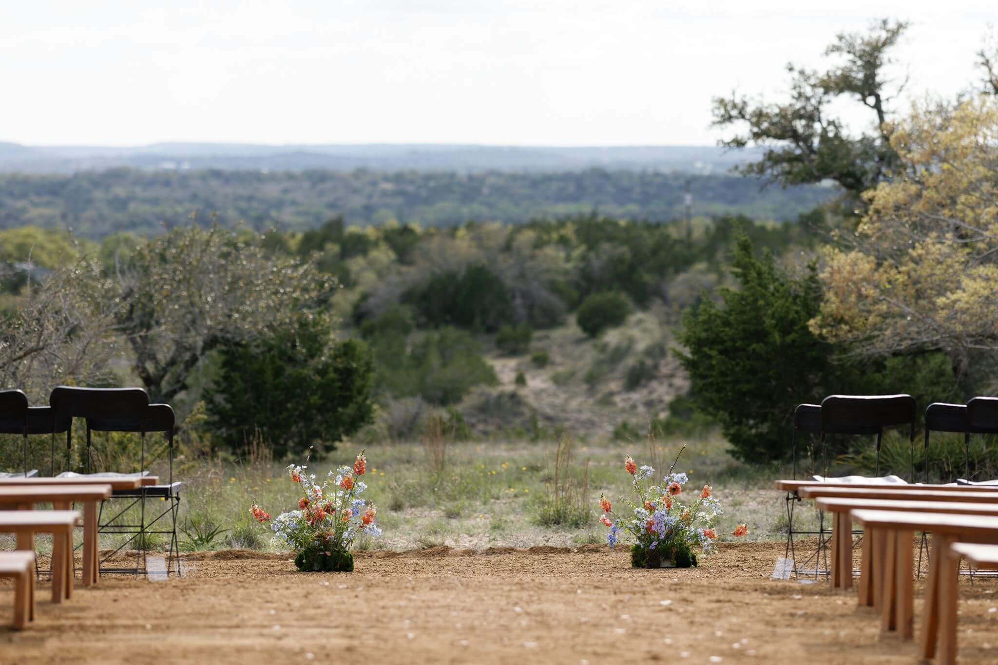 Rows of empty wooden ceremony benches set up overlooking the Texas Hill Country at sunset