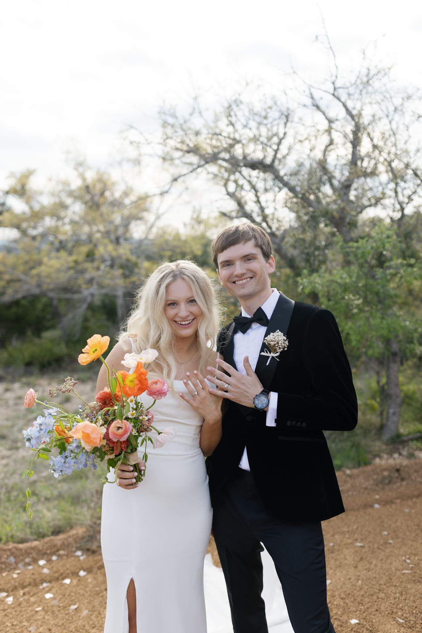 Bride and groom embracing outdoors, her holding a colorful wildflower bouquet