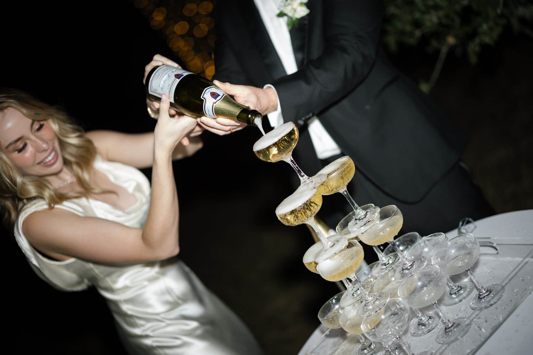 Close-up of champagne cascading through a tower of coupe glasses as the newlyweds pour from a bottle.