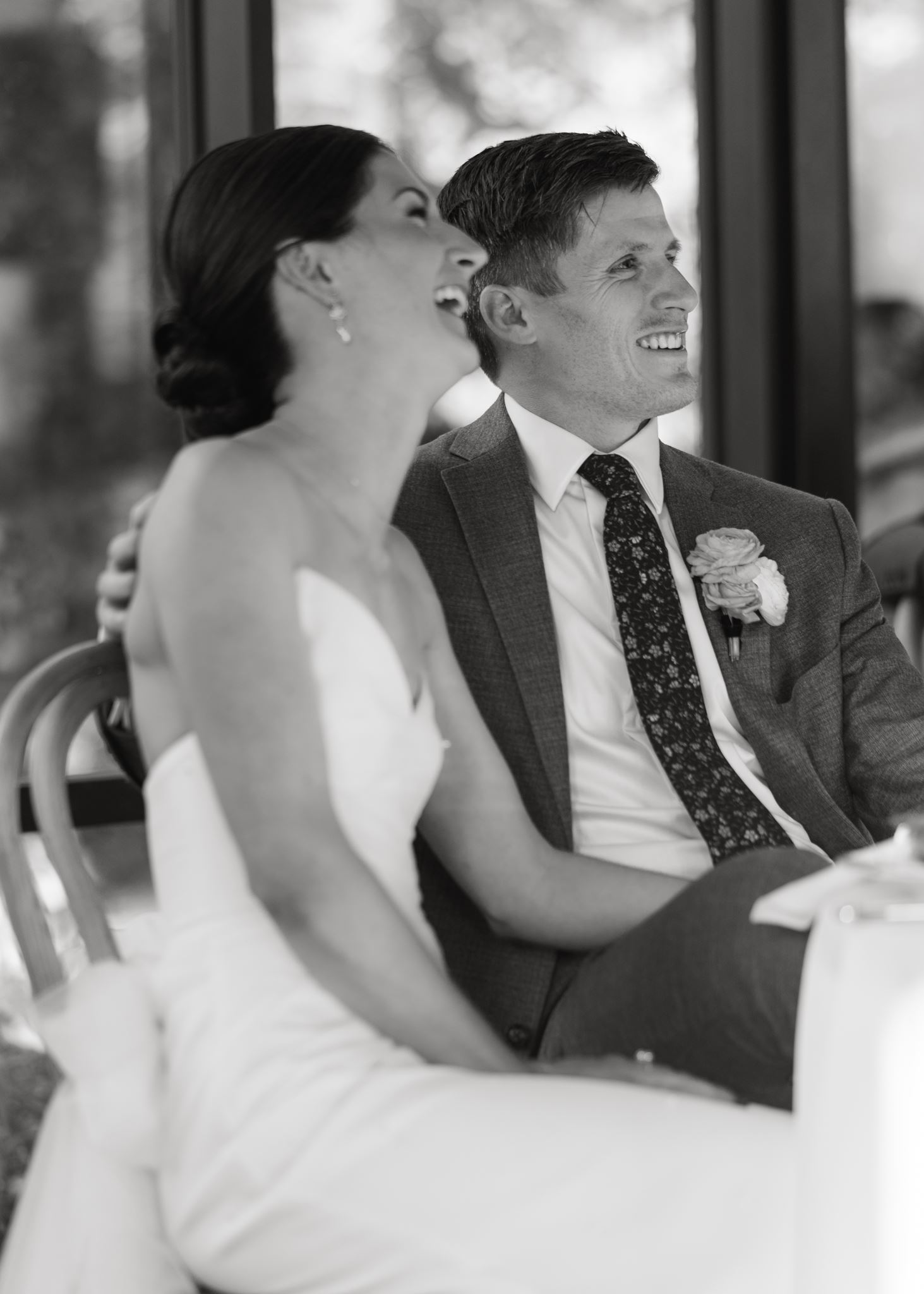 Black-and-white portrait of the bride and groom sitting closely together and smiling.