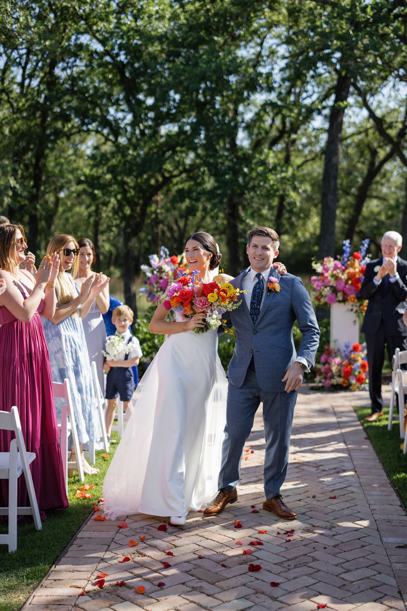 Newlyweds walking down the ceremony aisle as guests applaud around them.