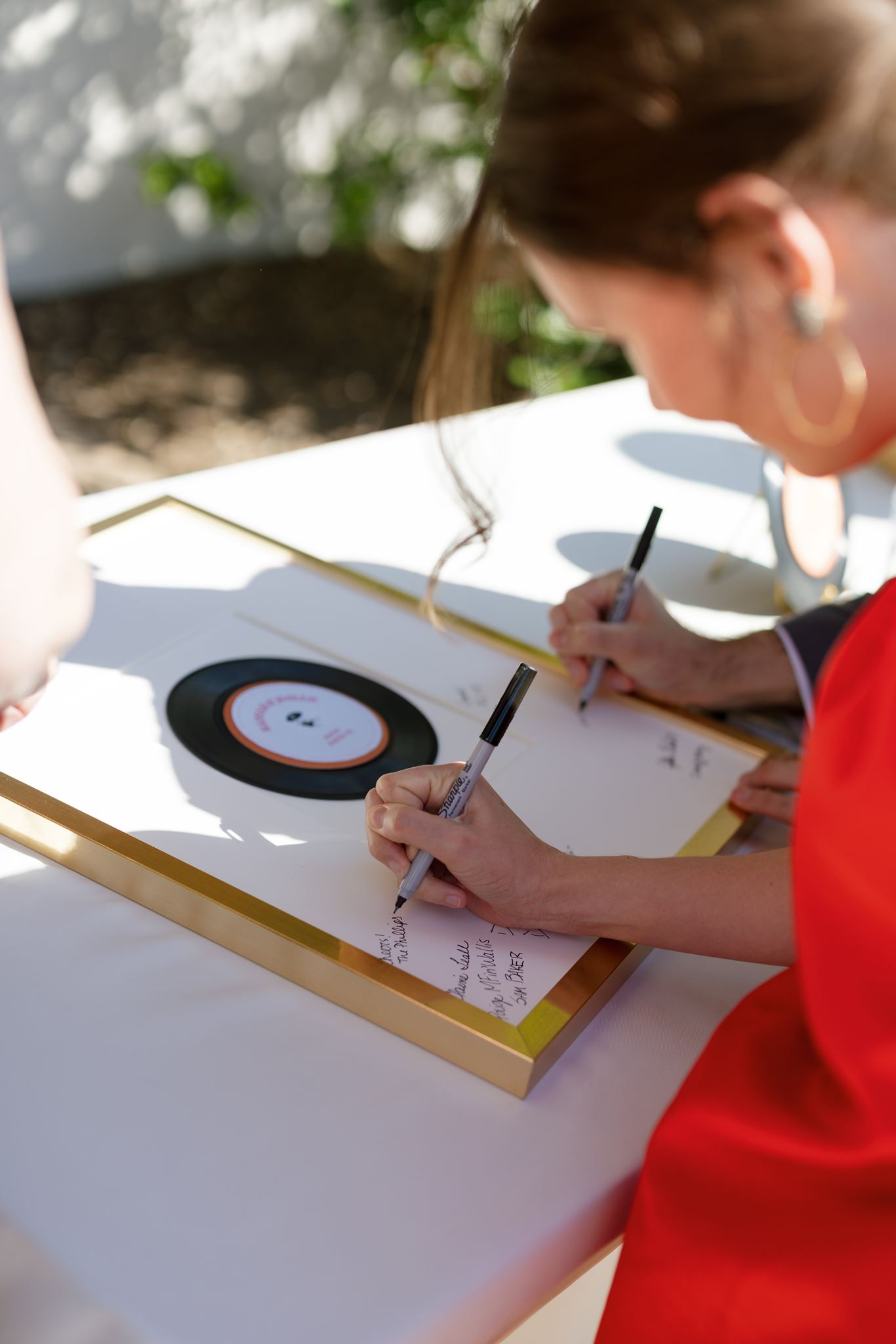 Guest signing a vinyl record guest book at an outdoor table during the wedding celebration.