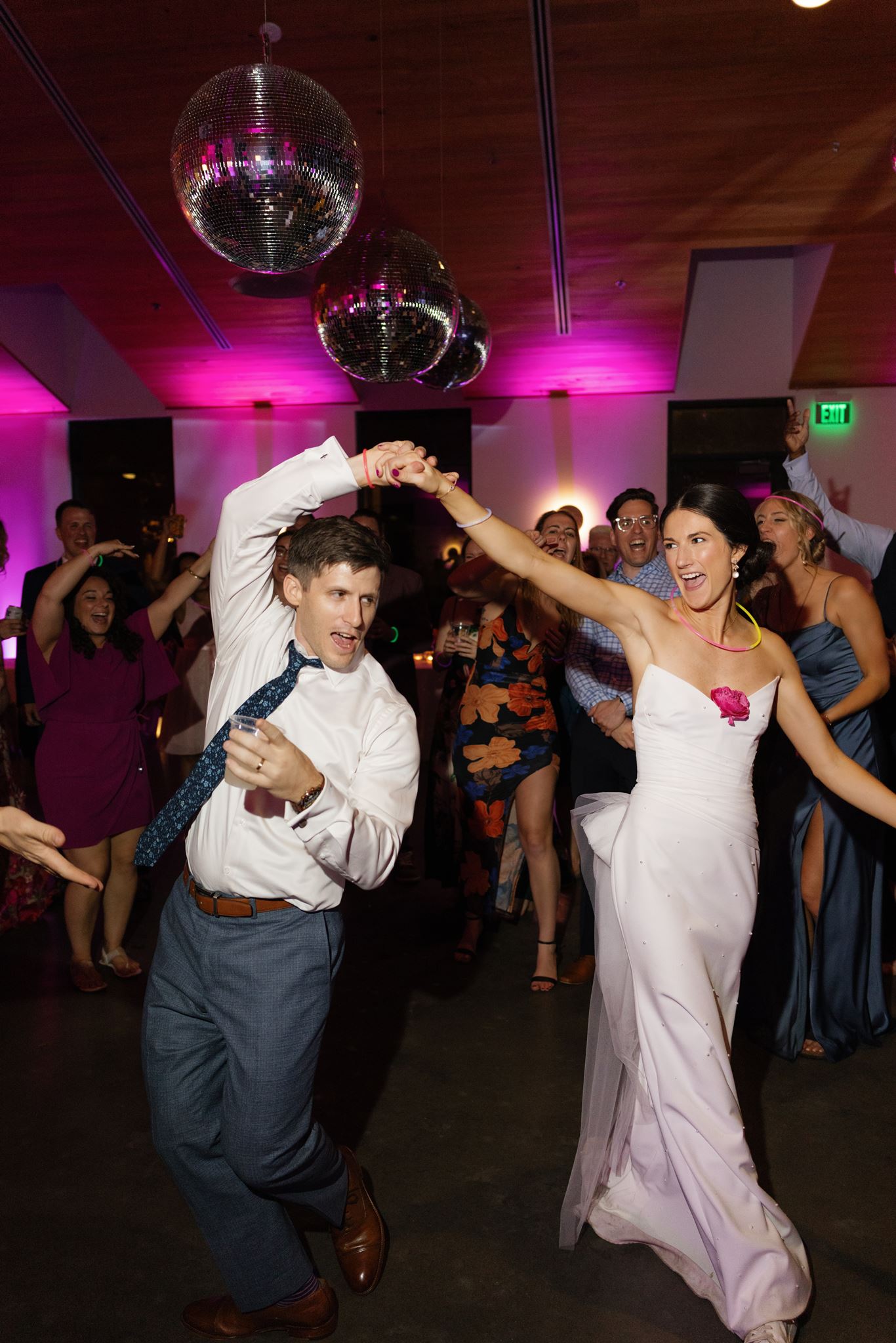 Bride raising her arm while dancing beside the groom and cheering guests at the reception.