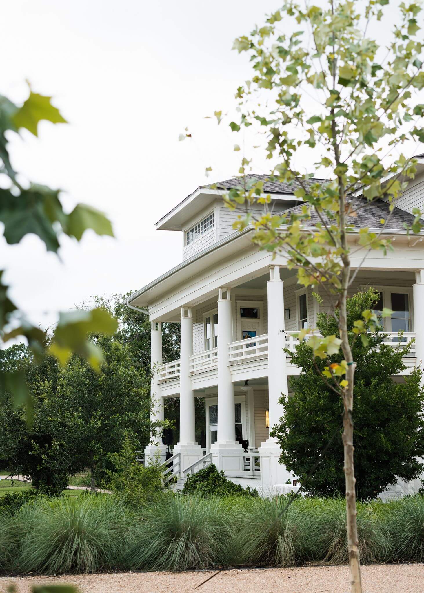 Exterior of a large white two-story wedding venue surrounded by trees and landscaped greenery.