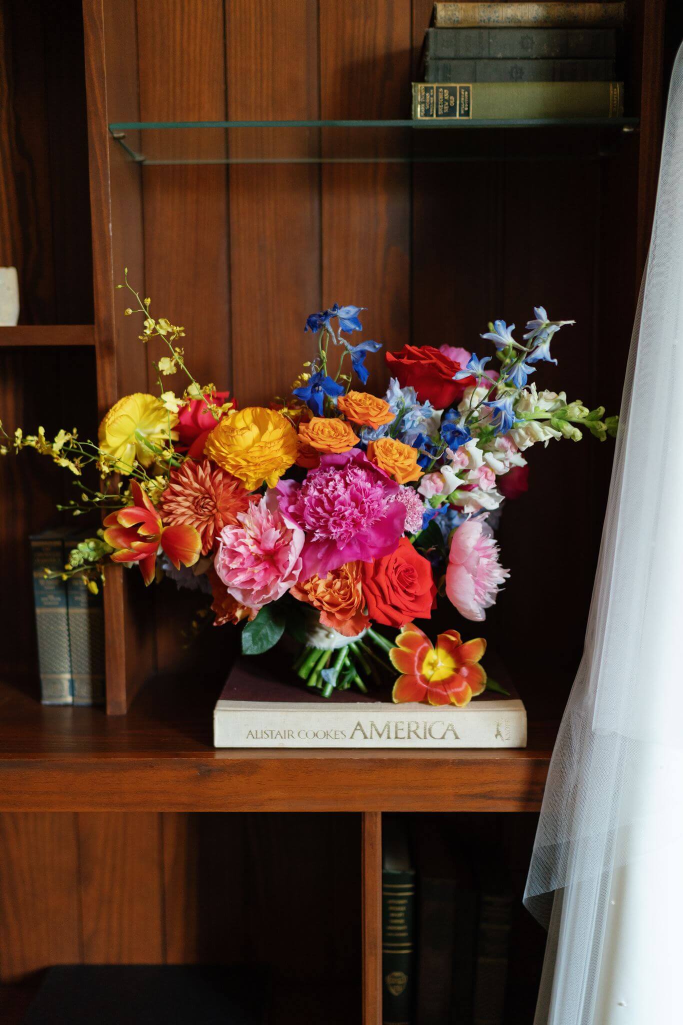Colorful bridal bouquet with red, pink, orange, yellow, and blue flowers displayed on a bookshelf inside The Grand Lady.