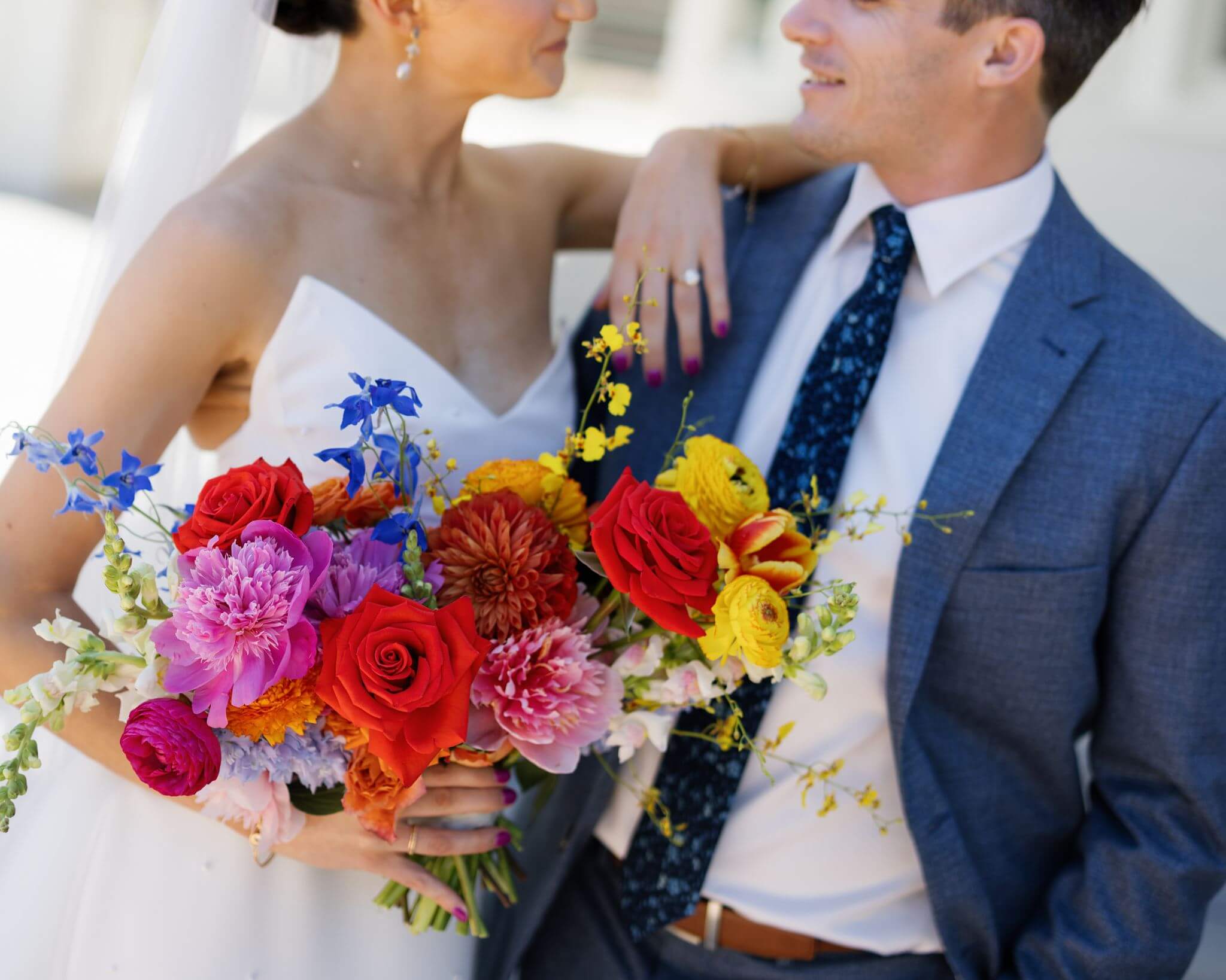 Close-up wedding portrait highlighting the bride’s colorful bouquet of red, pink, yellow, orange, and blue flowers at The Grand Lady.
