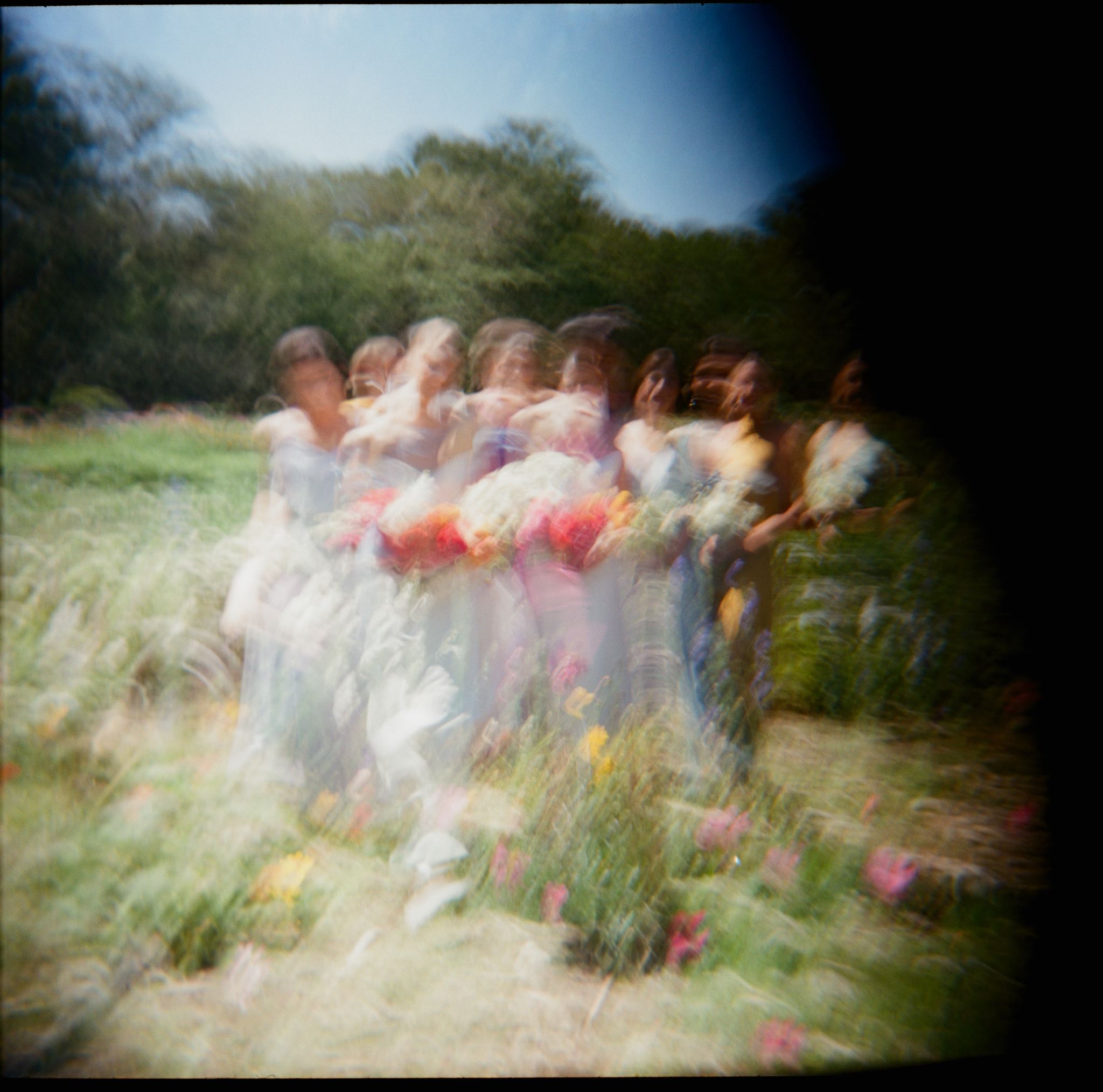 Dreamy motion-blur photograph of the bride and bridesmaids walking through a wildflower garden.