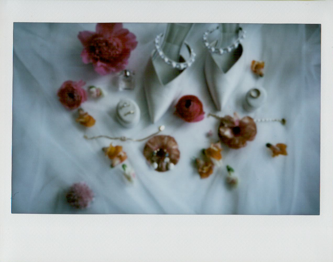 Polaroid-style flat lay of wedding stationery, jewelry, flowers, and small detail pieces.