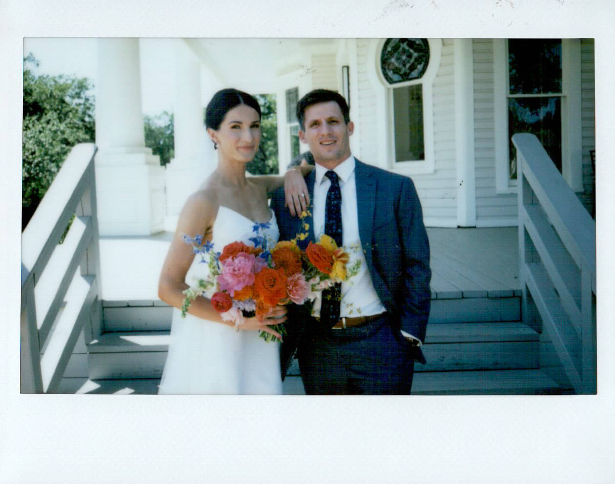 Polaroid-style portrait of the bride and groom with a colorful bouquet on the front porch of The Grand Lady wedding venue.