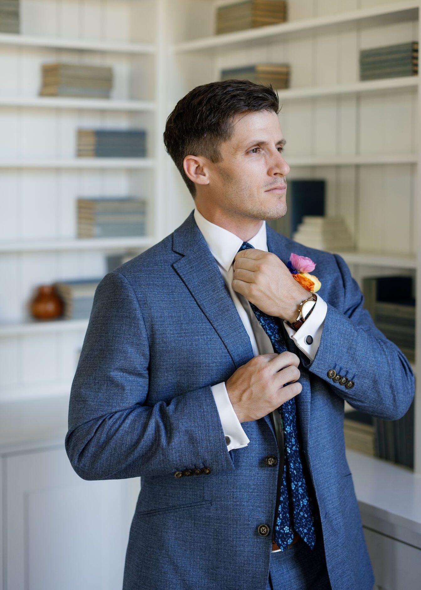Groom adjusting his tie while getting ready in a blue three-piece suit.
