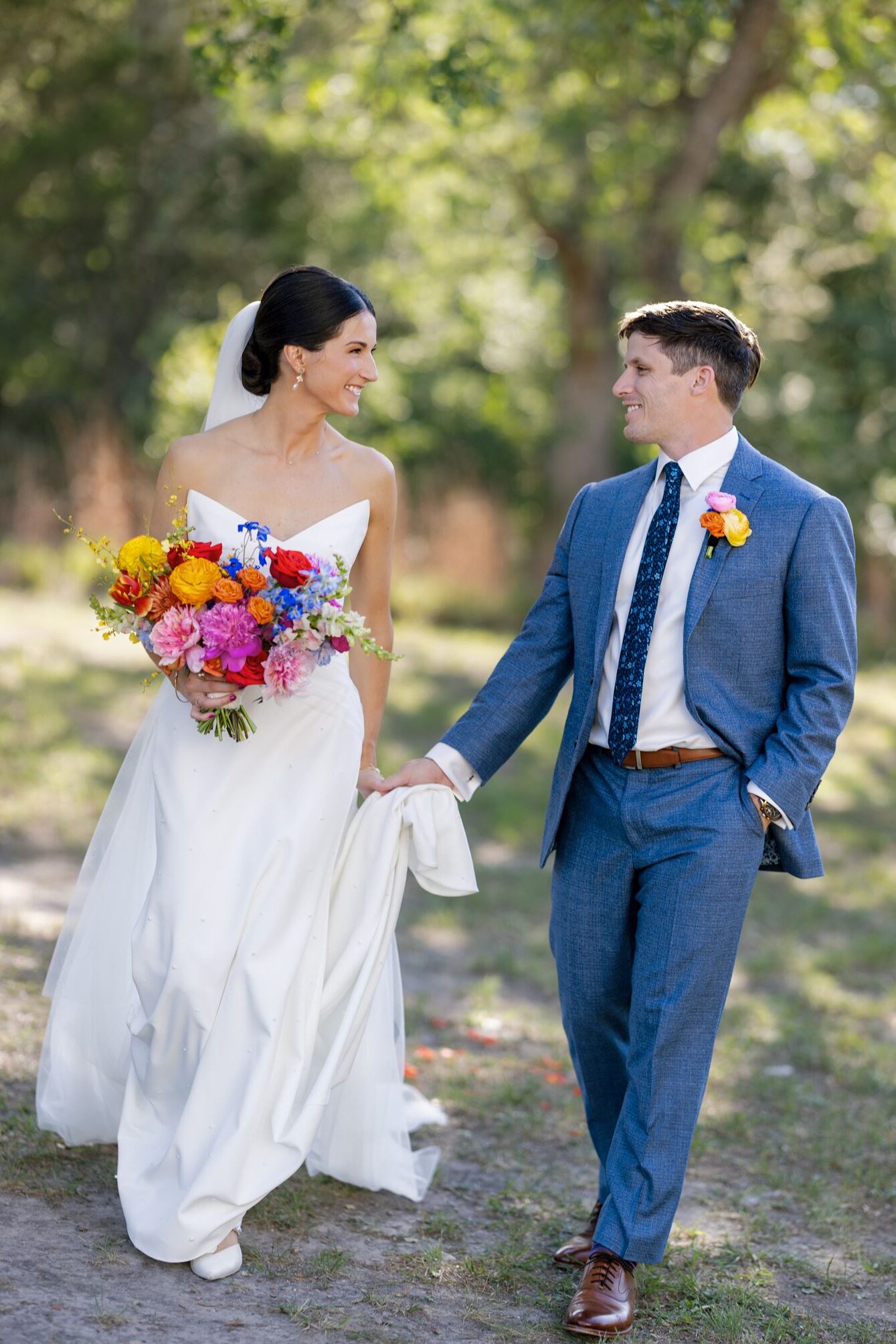 Groom holding his brides dress train as they walk towards the camera
