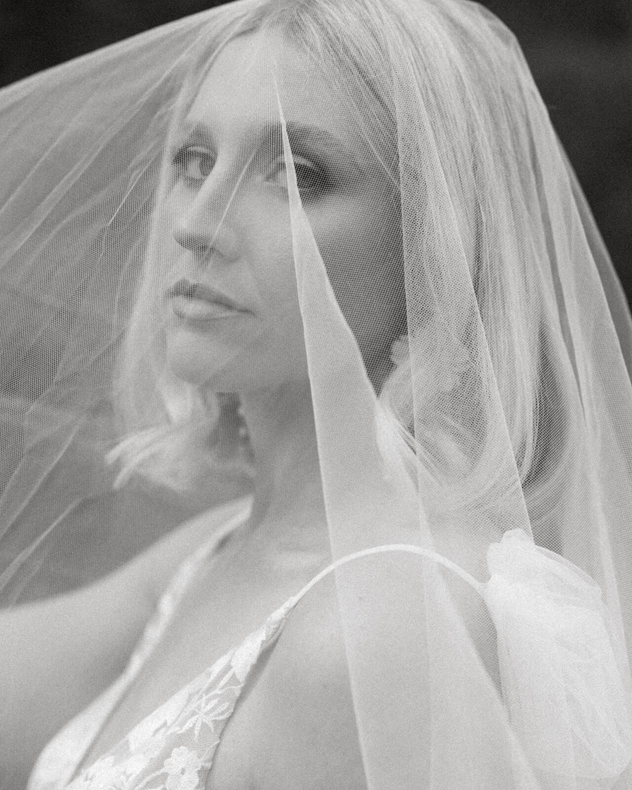 An artistic black-and-white close-up of a bride's face beneath her sheer wedding veil.